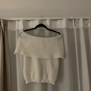 Vit offshoulder stickad tröja - Superfin vit stickad tröja med bred offshoulder-ringning som ger en snygg och trendig look. Mjuk och skön, perfekt att styla med jeans eller kjol. Ribbstickad struktur och elastisk nederkant för en bekväm passform.