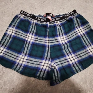 Rutiga blå-gröna shorts Hunkemöller XS - Säljer ett par mjuka och chill rutiga shorts från Hunkemöller i blått, grönt och vitt. Elastisk midja med DAY OFF-tryck och skön passform. Perfekta för att hänga hemma eller sova i. Klassisk loose fit och riktigt comfy vibe.