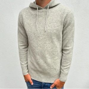 Ljusgrå stickad hoodie med huva - Mysig ljusgrå stickad hoodie med huva och snörning. Tröjan har lång ärm och ribbade muddar vid ärmslut och nederkant. Perfekt för dig som gillar en enkel och stilren look.