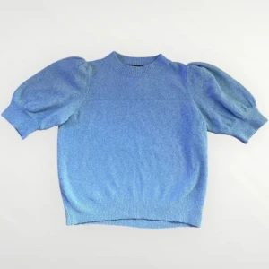 Blå stickad tröja med puffärm - Supersöt blå stickad tröja med korta puffärmar och ribbad halsringning. Perfekt för dig som vill ha en trendig och bekväm look. Tröjan har en mjuk känsla och passar lika bra till jeans som kjol. I storlek S från Vero Moda.