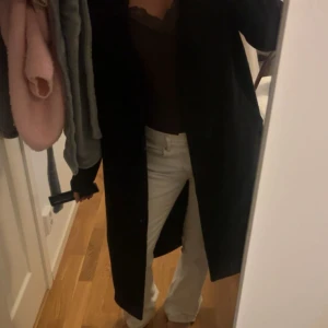 Svart lång kappa  - Säljer en svart, stilren och lång kappa med bälte i midjan. Jackan har en klassisk rak passform och långa ärmar, den är lite luddig och lite nopprig! Men går att ta bort med en noppermarskin… den är förövrigt väldigt fint skick. Använd en vår säsong🩷🩷