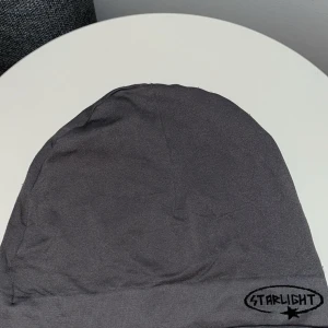 Grå mössa Starlight med tryck - Snygg grå mössa från Starlight med svart tryck på kanten. Enkel och stilren design med mjukt material som sitter skönt på huvudet. Perfekt för dig som gillar minimalistisk stil och vill ha något som funkar till alla outfits.