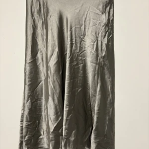 Silvrig långkjol från The Black Label - Snygg silvrig långkjol i glansigt satinliknande material från The Black Label Collection. Kjolen har en enkel och stilren design med diskret dragkedja i sidan. Perfekt för dig som vill ha en clean och trendig look. (Använt 1 gång tidigare) inte min stil, priset kan diskuteras.