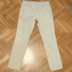 Beiga chinos - Snygga beiga chinos med slim fit. Byxorna har fickor fram och bak med knappstängning bak. Perfekta för en clean och stilren look. Materialet är mjuk och skön bomull. W31L31