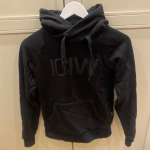 Svart hoodie från ICANIWILL - Svart hoodie från ICANIWILL i storlek XS med stor logga framtill och snygga snören i huvan. Tröjan har en klassisk känguruficka och mjukt material som passar perfekt för chill eller träning. Snygg och enkel design med lång ärm och ribbade muddar.