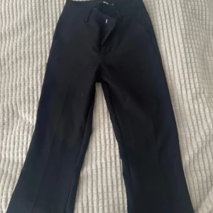 Svarta kostymbyxor med raka ben - Snygga svarta kostymbyxor med raka ben och klassiska fickor både fram och bak. Byxorna har hällor för bälte och är tillverkade i ett slätt tyg som känns dressat. Perfekta för en clean och stilren look.