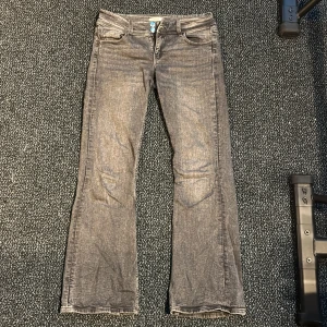 Grå bootcut jeans från Gina Tricot - Snygga grå, lågmidjade bootcut  jeans från Gina Tricot. Jeansen har klassisk femficksdesign, silverfärgade knappar. 
