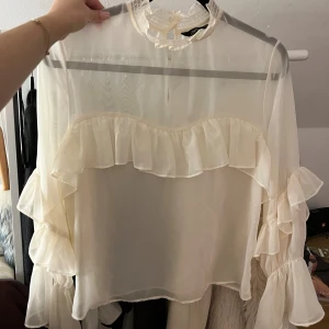 Vit volangblus från Zara - Supersöt transparent vit blus från Zara med volanger över bröstet och längs ärmarna. volangdetaljer och långa ärmar med flera lager volanger. 