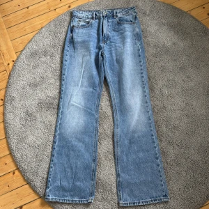 Blå straight jeans från Stradivarius - Snygga ljusblå jeans från Stradivarius i klassisk straight -modell. Jeansen har 4 fickor, vintage-inspirerad läderpatch bak och orangea sömmar. Materialet är jeans med en skön känsla och passformen är normal. Perfekt för dig som gillar retrostil och vill ha ett par jeans med lite extra stil.