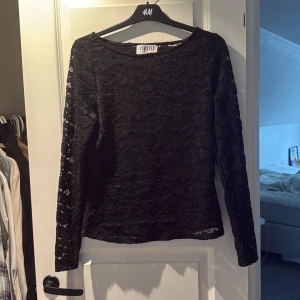 Svart spetsblus från AWARE, storlek L - Säljer en svart blus från AWARE i storlek L. Blusen har lång ärm och är helt täckt av blommig spets som ger en snygg och romantisk vibe. Rund halsringning och transparenta detaljer i spetsen gör den extra cool. Perfekt för dig som gillar stilrena och trendiga plagg.