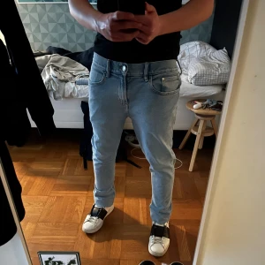 Ljusblå jeans från H&M - Säljer ett par ljusblå jeans med klassisk femficksdesign och slim fit. Jeansen har slim passform, dragkedja och knapp i midjan. Materialet är jeans med snygga sömmar och ljus tvätt. Perfekt för dig som gillar en clean och enkel stil. 100 cm i längd!