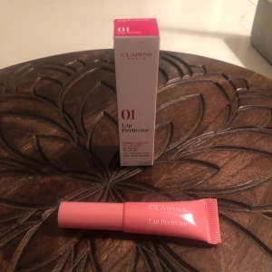 Clarins Lip Perfector 01 Rose - Clarins Lip Perfector i nyansen 01 Rose är ett läppglans med sheasmör som ger mjuka och glansiga läppar. Tuben är ljusrosa och har en praktisk applikator. Kommer i originalförpackning och är perfekt för dig som vill ha naturligt glansiga läppar.