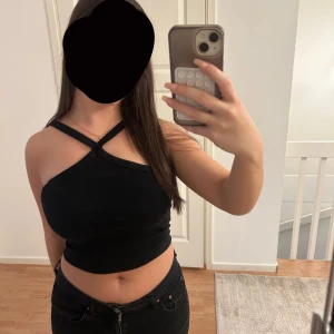 Svart croppad topp från Gina Tricot - Säljer en svart croppad topp från Gina Tricot med snygga korsade axelband och tight passform. Toppen är ärmlös och har en stilren look som passar perfekt till jeans eller kjol. Materialet är mjukt och stretchigt för en bekväm känsla.