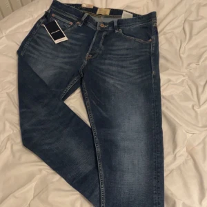 Jack & Jones blå jeans 32/32 tapered - Snygga blå jeans från Jack & Jones i modellen JJIerik JJcole CB 125. Jeansen har en klassisk femficksdesign, tapered fit och normal midja. Materialet är slitstarkt denim i bomull med snygga slitningar och kontrastsömmar. Perfekta för en avslappnad och trendig look.