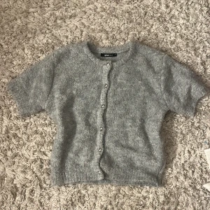 Grå stickad kofta från Gina Tricot - Mysig grå stickad kofta från Gina Tricot i storlek XS. Kortärmad modell med rund halsringning och knappar framtill. Perfekt att slänga över en topp för en chill look. Supermjuk och fluffig känsla. Helt i nyskick och aldrig kommit till användning💞💞