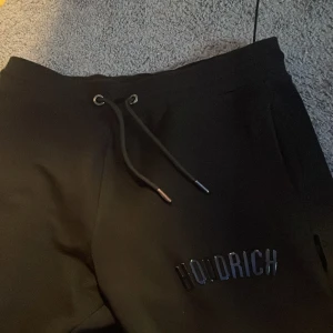Svarta mjukisbyxor från Hoodrich S - Svarta mjukisbyxor från Hoodrich i storlek S. Byxorna har dragsko i midjan och Hoodrich-logga framtill. De är raka i modellen och tillverkade i mjukt material som är skönt att ha på sig. Perfekta för en chill och avslappnad stil.