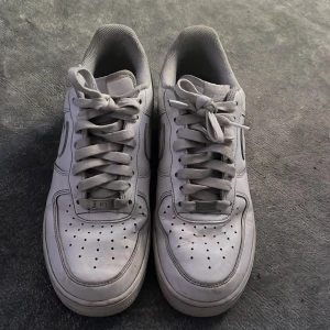 Nike Air Force 1 vita sneakers herr - Säljer ett par klassiska Nike Air Force 1 sneakers i helvitt skinn med rund tå och platt sula. Skorna har snörning och den ikoniska swoosh-loggan på sidan. Perfekt för dig som gillar stilrena och tidlösa sneakers. Storlek 42.5. Säljer dom då dom inte passar mig längre.