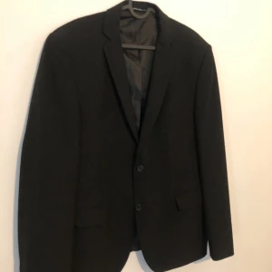 Svart klassisk kavaj - En stilren svart kavaj från H&M med två knappar framtill och klassiska slag. Kavajen har raka ärmar och två fickor med lock. Perfekt för en dressad look och passar till många olika outfits.