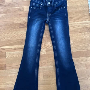 Bootcut jeans från RYVLS Stockholm - Snygga mörkblå bootcut jeans från RYVLS Stockholm i storlek 164. Jeansen har kontrasterande vita sömmar, klassisk femficksdesign och en cool tvätt med ljusare partier framtill och baktill. Materialet är jeans med dragkedja och knapp framtill.