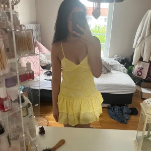 Gul- och vitrutigt sommarklänning  intressekoll  - Supersöt kort klänning  i gul- och vitrutigt mönster. Smala axelband, volangkant nertill och knytning i ryggen. Figurnära passform upptill och luftig kjol. Perfekt för varma dagar och ger en fräsch vibe. Intressekoll