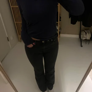 Svarta bootcut jeans med hög midja - Snygga svarta jeans med bootcut passform och hög midja. Klassisk femficksmodell med knapp och dragkedja framtill. Jeansen har en rak siluett upptill och lätt utsvängda ben, vilket ger en cool och tidlös look.