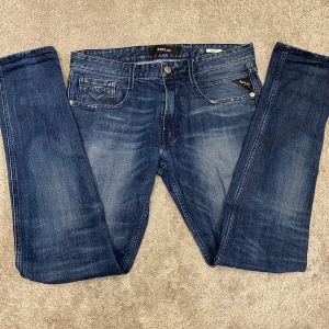 Replay Anbass Jeans  - Säljer ett par snygga Replay Anbass jeans i mörkblå tvätt med diskreta slitningar. Modellen har smal passform, klassiska fem fickor och logga på myntfickan. Jeansen är tillverkade i stretchig bomullsdenim för extra komfort och sitter riktigt bra.