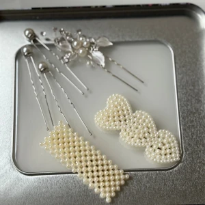 Set med pärlhårnålar och hårspännen - Snyggt set med hårnålar och hårspännen dekorerade med vita pärlor och silverfärgade detaljer. Ett hårspänne har hjärtformad design med pärlor, det andra är rektangulärt med pärlor. Hårnålarna har pärlor och blommiga silverdetaljer med små kristaller. Perfekt för att ge din frisyr extra stil.