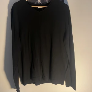 Svart v-ringad tröja från Filippa K - Minimalistisk svart v-ringad tröja från Filippa K i storlek M. Tröjan har lång ärm och en clean look utan synliga detaljer, perfekt för dig som gillar stilren design. Tillverkad i mjukt material som känns skönt mot huden.