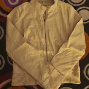 Retro jacka Asian size M  - Snygg beige skinnjacka med ribbad nederkant och metallknappar vid fickorna. Jackan har en rak passform, lång ärm och stängs med dragkedja framtill. Perfekt för dig som gillar stilrena och cleana plagg med lite edge.