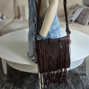 Läderväska med fransar * hippie / bohem * nyskick - Perfekta julklappen! Unik mörkbrun läderväska/axelremsväska med flätat mönster och långa fransar.  * Justerbar axelrem.  * Ett fack med dragkedja på insidan samt ett utan.  * Nyskick. Använd två ggr (för många väskor)  * Höjd 28 cm, bredd 26 cm. Exkl fransarna.   Djur och rökfritt hem. Se bilder och förstora då de ingår i beskrivningen.  Se gärna mina övriga annonser. 