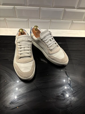 Burberry vita sneakers med rutigt bakstycke - Snygga vita sneakers från Burberry med klassiskt rutigt bakstycke i blått och vitt. Burberry-logga på plösen, Perfekta för dig som gillar stilrena och exklusiva sneakers.  Stora i storleken så passar mig med 41 men kan nog även stäcka sig till 42. Äkthets bevis , skobox och allt därtill finns med. 