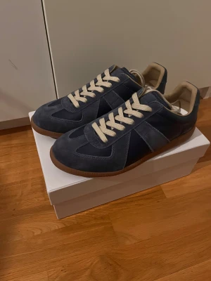 Maison margiela - Snygga sneakers i mörkblå mocka och skinn med beige snörning och innersula. Skorna har en klassisk siluett med gummisula i brunt och rund tå. Perfekta för dig som gillar stilrena och tidlösa sneakers med en modern touch. Inte orginale