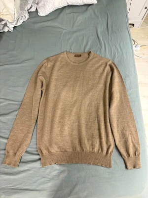 Beige stickad tröja från Stenströms - Snygg beige stickad tröja från Stenströms i storlek L. Tröjan har rund hals, långa ärmar och ribbade muddar vid ärmslut och nederkant. Diskret broderad logga på nedre delen. Perfekt för dig som gillar klassisk och clean stil.