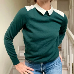 Grön tröja med vit krage från H&M - Stilfull grön långärmad tröja från H&M. Baksidan är i ett vitt tunnare tyg med panel och söt knapp vid nacken. Tröjan är i mjukaste ullblandning och har en klassisk välskräddad stil. Perfekt både vardag och mer uppklätt, supersnygg både till jeans, kostymbyxa och kjol, passar året om. Lätt att bära även under en kavaj. Modellen på bilderna är strl 36/S.