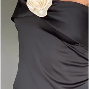 Viral Svart satin tubtopp med blomma från Motel Rocks - Supersnygg svart tubtopp i satin med en ljus, dekorativ blomma framtill. Toppen är axelbandslös och har en elegant, glansig finish som ger en lyxig vibe. Perfekt för dig som vill sticka ut med en unik detalj och stilren look. Kan skicka redan samma dag och du beställer innan kl 8 på morgonen. Skick enligt bild, blomman är lite grå från tvättning. Endast provad. Kommer inte sänka priset. Slutsåld överallt. Nypris 40 euros ~ 439 sek. Blomman är lite grå på grund av tvättning