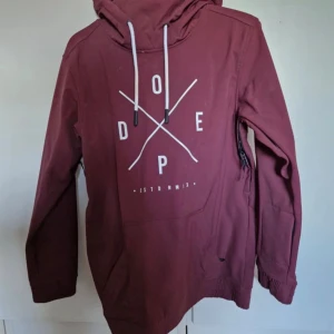 Vinröd vindjacka från Dope, S - Säljer en vinröd skidjacka, funkar även som vanlig jacka. från Dope med stor vit logga på bröstet och coola snören i huvan. Jackan har lång ärm, dragkedja i sidan och mjukt fleecefoder insidan. Har aldrig använt den, skulle iväg på skidhelg med mina vänner men blev aldrig av så den har bara hängt. Vill inte slänga något som är orört, när någon annan kan behöva den o låta den komma till användning. 🫶🏻                                                 Nypris: 1699 kr. 