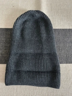 Mörkgrå ribbad mössa från Doppelgänger - Snygg mörkgrå mössa från Doppelgänger Roma, tillverkad i 100% akryl. Den har en klassisk ribbstickad design med uppvikt kant som ger en chill och stilren look. Perfekt för kalla dagar när du vill hålla dig varm och samtidigt se cool ut. Helt ny utan prislapp. Köpt i Italien 🇮🇹.