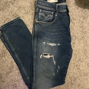 Replay Hyperflex blå jeans med slitningar - Snygga Replay Hyperflex jeans i mörkblå tvätt med slitna detaljer på framsidan. Klassisk femficksmodell med raka ben och broderade bakfickor. Stretchigt material för skön passform. Anbass modell, HELT OANVÄNDA! Vid frågor är det bara att hör av sig!🫡