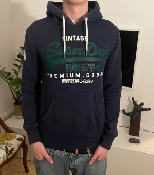 Mörkblå Superdry hoodie - Snygg superdry hoodie i storlek S. Modellen är 187cm. Hör av dig vid minsta fundering
