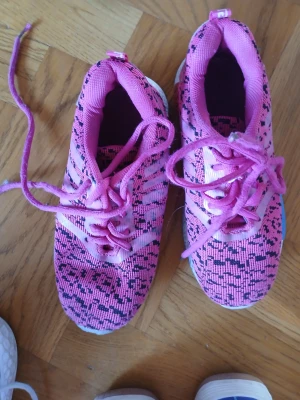 Rosa Adidas sneakers med mönster - Säljer ett par rosa Adidas sneakers med svart mönster och vita detaljer. Skorna har klassiska tre ränder på sidan, snörning och en bekväm, vit sula. Ovandelen är i syntetmaterial och mesh för bra andningsförmåga. Perfekta för dig som gillar färg och sportig stil.
