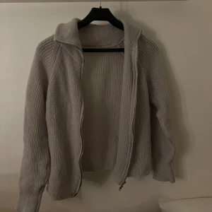 Beige stickad cardigan jacka/kofta - Mysig beige stickad cardigan jacka med dragkedja framtill och hög krage. Jackan har långärmade ribbade ärmar och en loose passform.  Pris kan alltid diskuteras + jag tar ej ansvar för postens slarv 🫶🏼