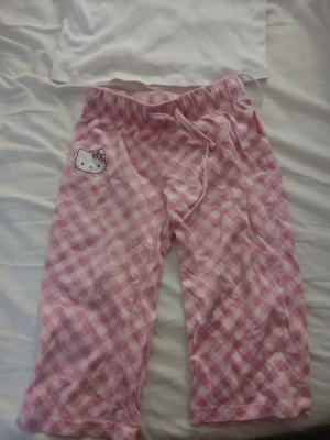 Hello Kitty pyjamas rosa/vit - Byxor i rosa och vitt rutmönster med Hello Kitty-detalj och dragsko i midjan. Perfekt för mysiga kvällar hemma. (OBS, Det är inte ett set, linnet går att köpa separat, men notera att det inte är samma storlek i byxorna och linnet)