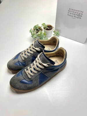 Maison Margiela blå och grå sneakers - Jag säljer nu mitt vackra par Maison Margiela Gats. De är begagnade men har fortfarande mycket att erbjuda. Utsidan av skon har knappt någon synlig användning, men ner till sulan och insidan av skon kan man se att den har använts och visar tecken på användning. Skorna är äkta och jag har ett kvitto som jag kan visa om du ber om det privat. Original låda medföljer också och jag skickar inom 24 timmar. Om du har några frågor, kom privat! ⚡️🦈