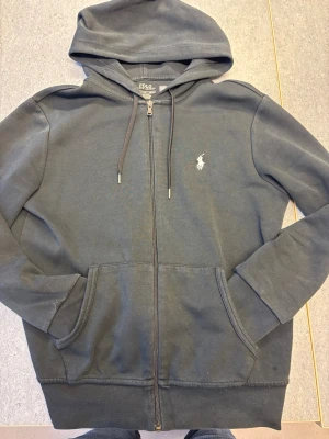 Svart hoodie från Polo Ralph Lauren - Klassisk svart hoodie från Polo Ralph Lauren med dragkedja framtill. Köpt för 1800 kr. Helt nytt skick har användt den 3 gånger 