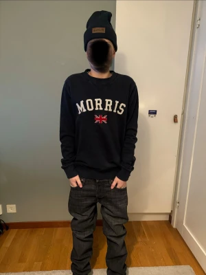 Svart Morris sweatshirt med tryck xs/s - Snygg svart sweatshirt från Morris med stort vitt tryck och Union Jack-flagga på bröstet. Tröjan har rund hals, långa ärmar och ribbade muddar. Perfekt för en avslappnad och stilren look.