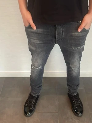 Mörkgrå slim jeans med slitningar - Snygga mörkgrå jeans med slitna detaljer och lätt tvättad look. Modellen är slim och sitter tajt längs benen. Perfekta för en trendig och avslappnad stil. Klassisk femficksdesign och tillverkade i stretchigt jeanstyg.