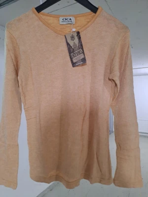 Beige långärmad topp från CICA - En stilren beige långärmad topp från CICA. Toppen har rund halsringning och är tillverkad i ett mjukt material som känns skönt mot huden. Perfekt att matcha med jeans eller kjol för en enkel och snygg look.