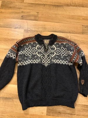 Mörkblå stickad tröja Dale of Norway - Säljer en mörkblå stickad tröja från Dale of Norway med klassiskt nordiskt mönster i vitt och inslag av rött och orange på axlarna. Tröjan har en half zip-dragkedja vid halsen och långärmad passform. Perfekt för kalla dagar och riktigt snygg retrostil.