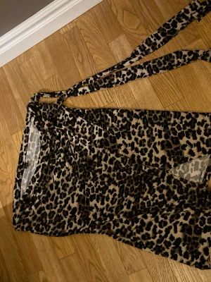 Leopardmönstrad omlottkjol med knyt - Snygg leopardmönstrad omlottkjol med långa knytband i midjan. Kjolen är i ett tunt, lätt material som känns perfekt för varma dagar. Beige och svarta toner ger ett trendigt intryck och den omlottade designen gör den enkel att justera. Kjolen är i storlek L men passar mig som har S i storlek.