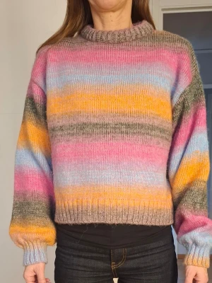 Flerfärgad randig stickad tröja - Säljer en stickad tröja med breda ränder. Tröjan har en rak, boxig passform, ribbad halsringning samt muddar vid ärmslut och nederkant. Perfekt för dig som gillar färg och en avslappnad stil.